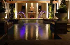 Swimming pool with white down lights highlighting the columns of a summer kitchen structure beyond
